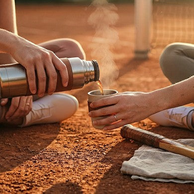 Pouring coffee from a flask into a cup on a clay court