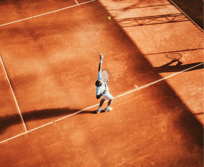 Tennis player serving on a red clay court, seen from above